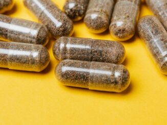 A photo of see-through herbal capsules with brown colored contents lying on a yellow background